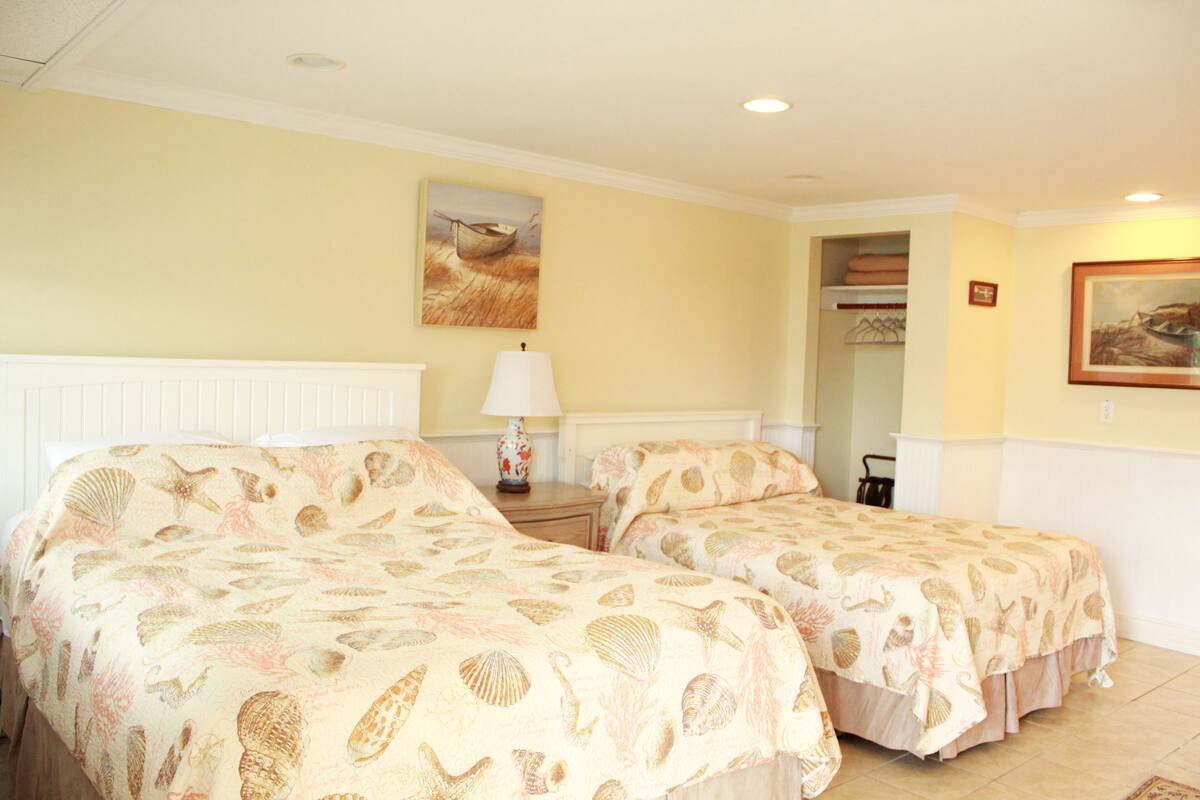 A hotel room with two beds, a nightstand with a lamp, a painting on the wall, and a closet.