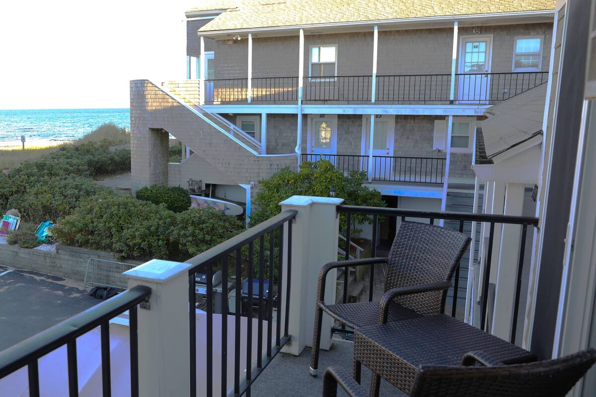 A balcony with wicker chairs, a view of the ocean, and a building with multiple balconies.