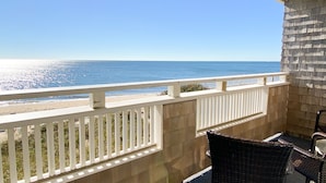 Un balcon abrité offrant une vue sur l’océan, avec une balustrade blanche et deux fauteuils en osier.