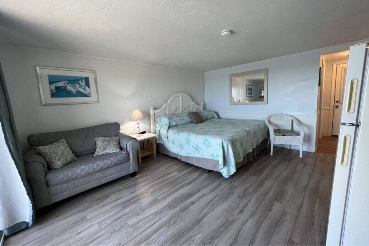 A bedroom with a bed, a sofa, a chair, a nightstand, a mirror, and a refrigerator.