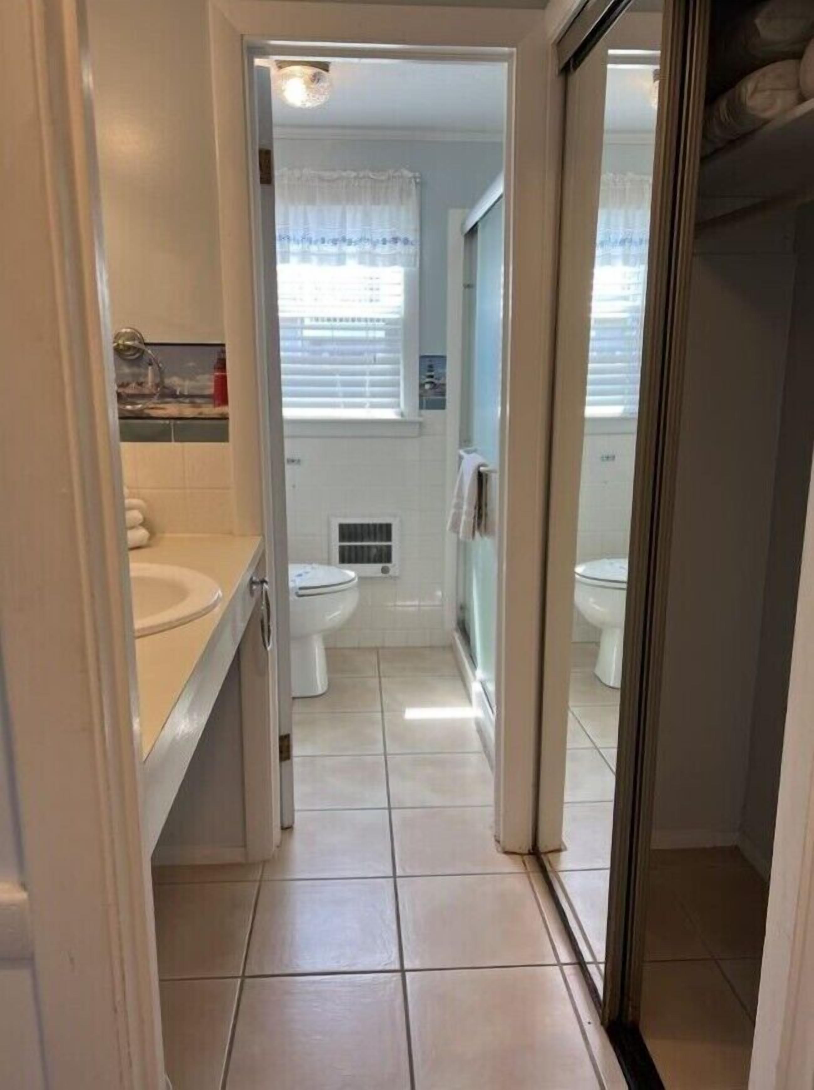 A narrow bathroom with a toilet, sink, and shower area.