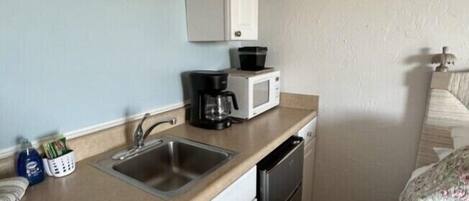 Una cocina compacta con un lavamanos, cafetera, microondas y lavavajillas.