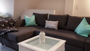Ein modernes Wohnzimmer mit einem dunkelbraunen Sofa, Kissen in Türkis und Weiß sowie einem kleinen weißen Beistelltisch mit einer transparenten Glasplatte.