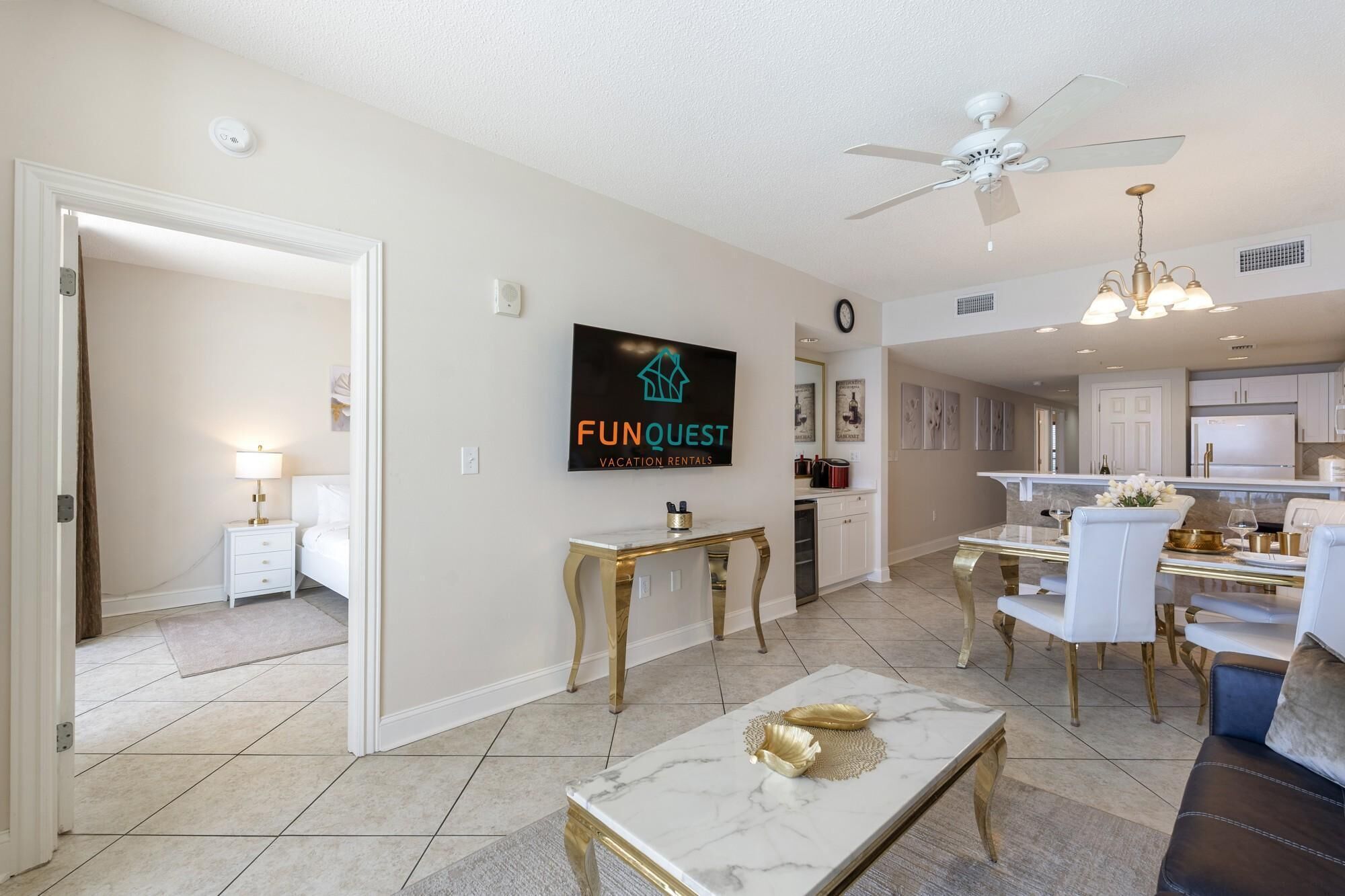 A spacious living area with a dining table, a TV mounted on the wall, and a kitchen in the background.