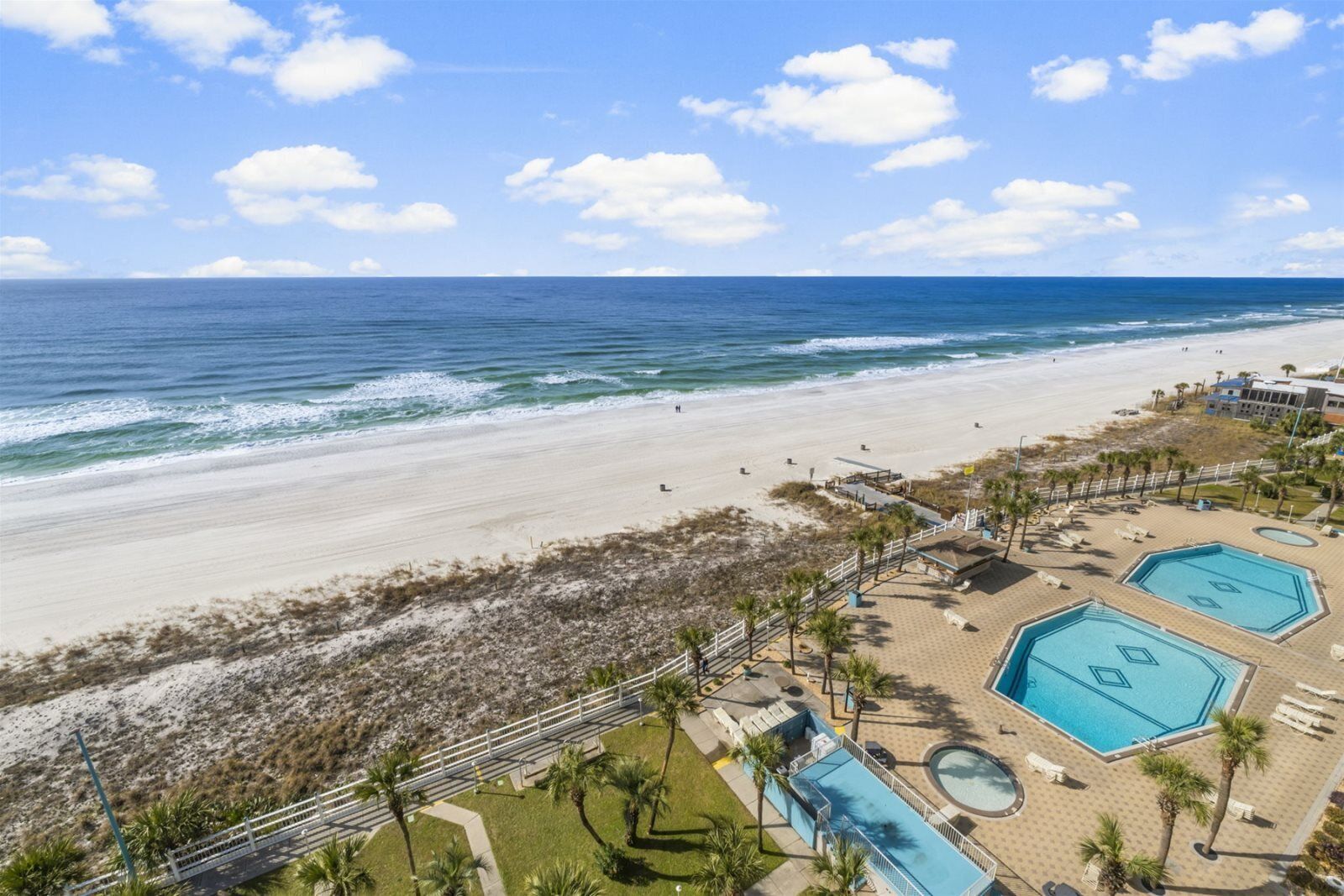A beach resort with a pool area, palm trees, and a view of the ocean.