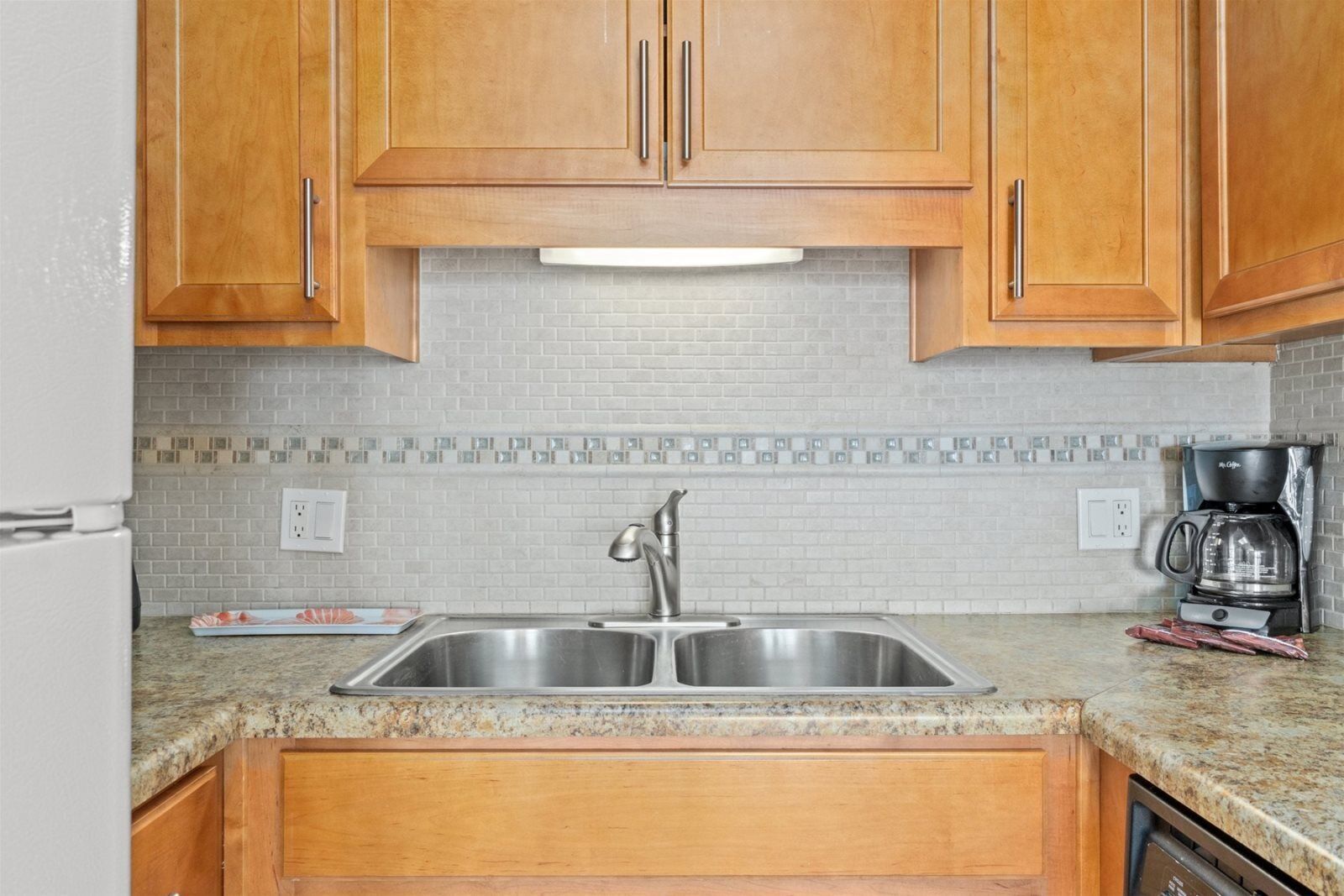 A kitchen with wooden cabinets, a stainless steel sink, a coffee maker, and a dishwasher.