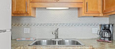 A kitchen with wooden cabinets, a stainless steel sink, a coffee maker, and a dishwasher.