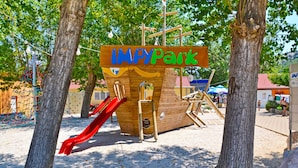 En lekplats med en lekställning i form av ett träpiratskepp, en röd rutschkana och en skylt med texten ”IMPYPark”.