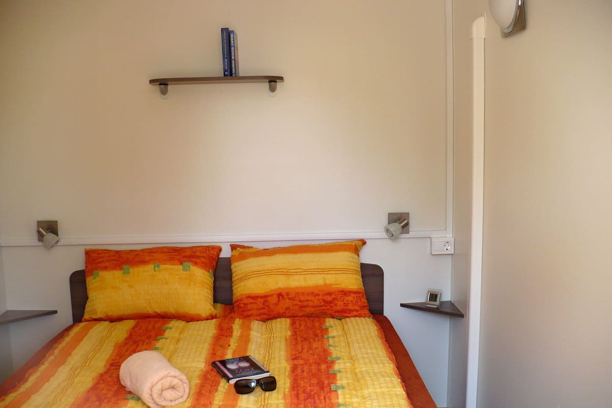 A neatly made bed with a striped bedspread, two pillows, a folded towel, and a book with sunglasses on it.