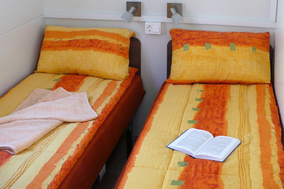Two single beds with orange and yellow striped bedding, a small shelf above, and a book on one bed.