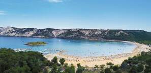 A coastal beach with clear waters, a sandy shore, and a mountainous backdrop.