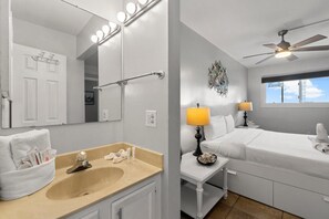 A bathroom with a sink, mirror, and vanity. There is a towel rack with towels and toiletries. The room has a ceiling fan and a window with a view of the sky.
