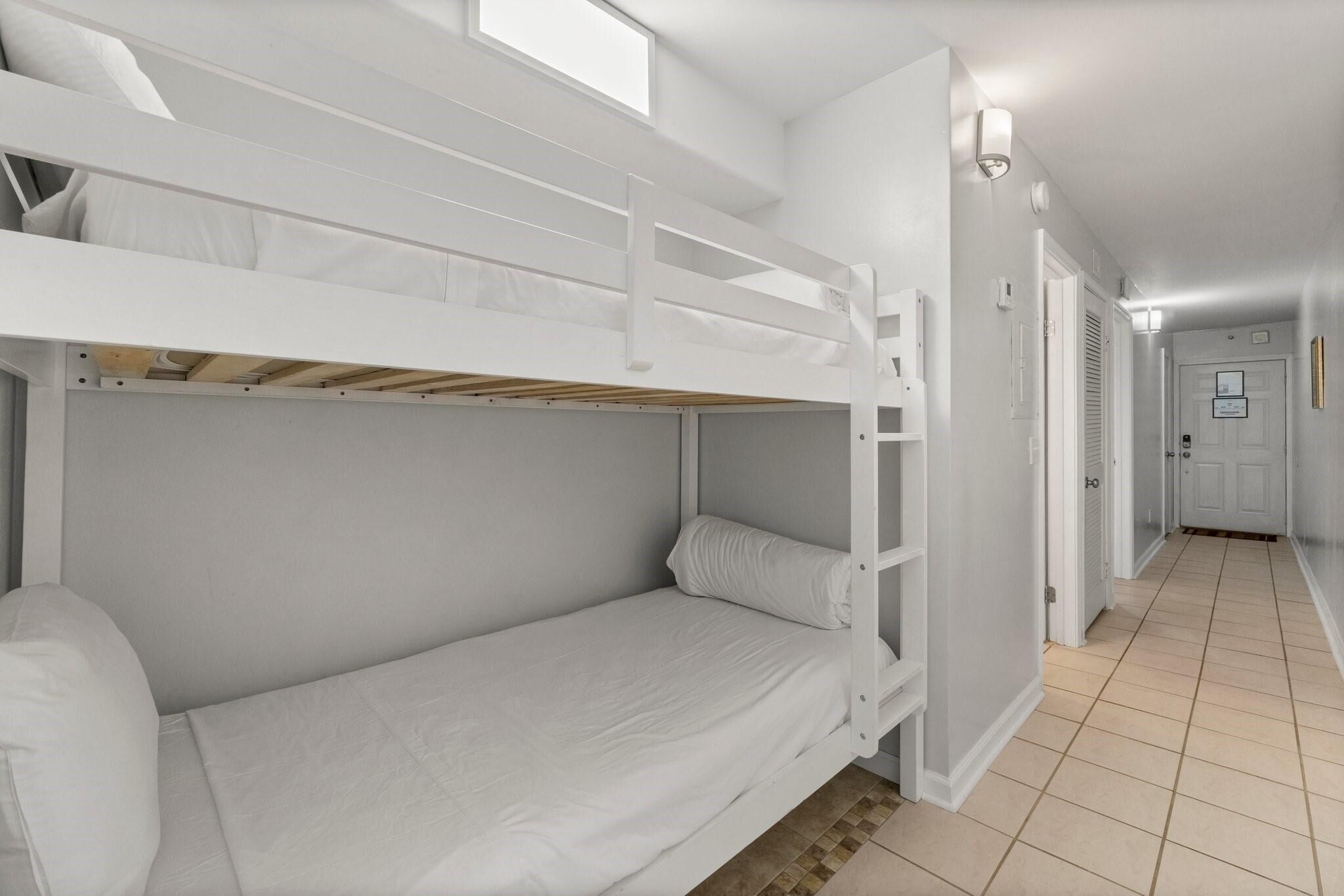 A bunk bed room with a skylight, a hallway with doors, and a tiled floor.