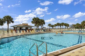 Une piscine avec des chaises longues, un bar et des palmiers.