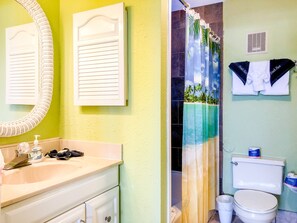 Une salle de bain équipée de toilettes, d’un lavabo et d’un rideau de douche à motifs tropicaux.