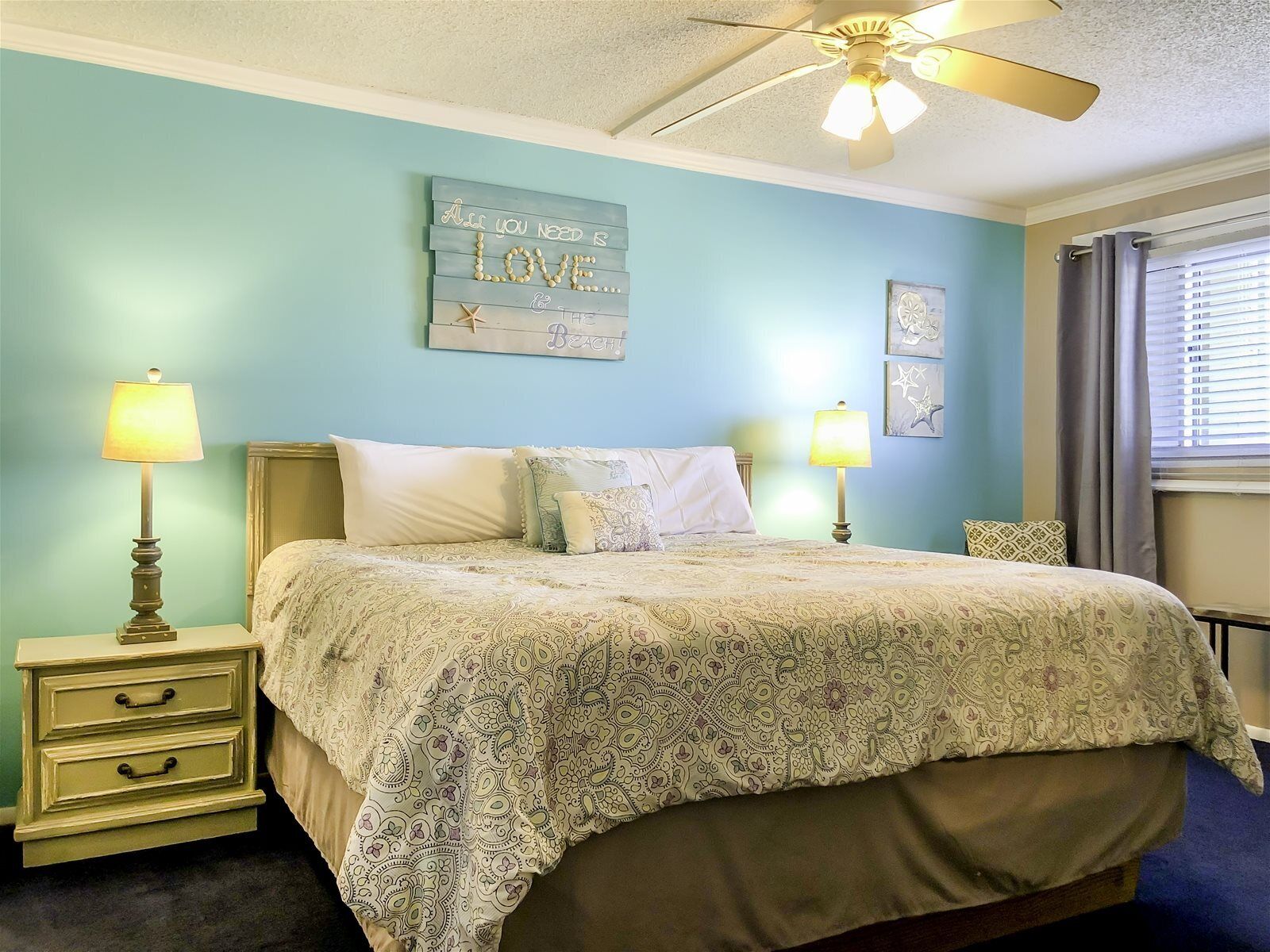 A bedroom with a bed, two bedside tables, a ceiling fan, and a wall decoration.