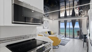 A modern kitchen with a built-in oven and stovetop, a dining area with a yellow chair, and a balcony with a view of the ocean. - The Summit 702 (Panama City Beach)
