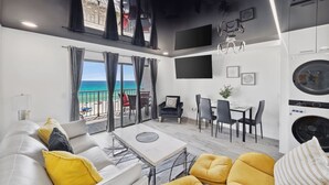 A modern living room with a balcony overlooking the sea, a dining area, and a kitchen with appliances. - The Summit 702 (Panama City Beach)