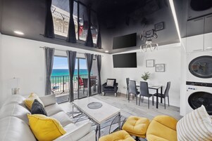 Un salon moderne avec balcon donnant sur la mer, un coin repas et une cuisine équipée.