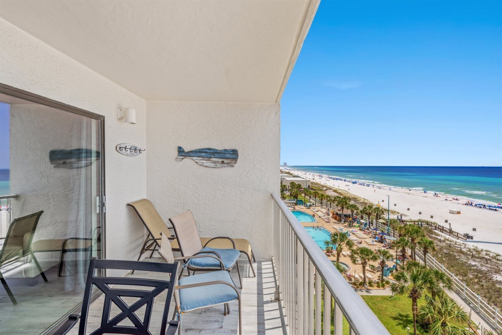 A balcony with a view of a beach, lounge chairs, and a pool area.