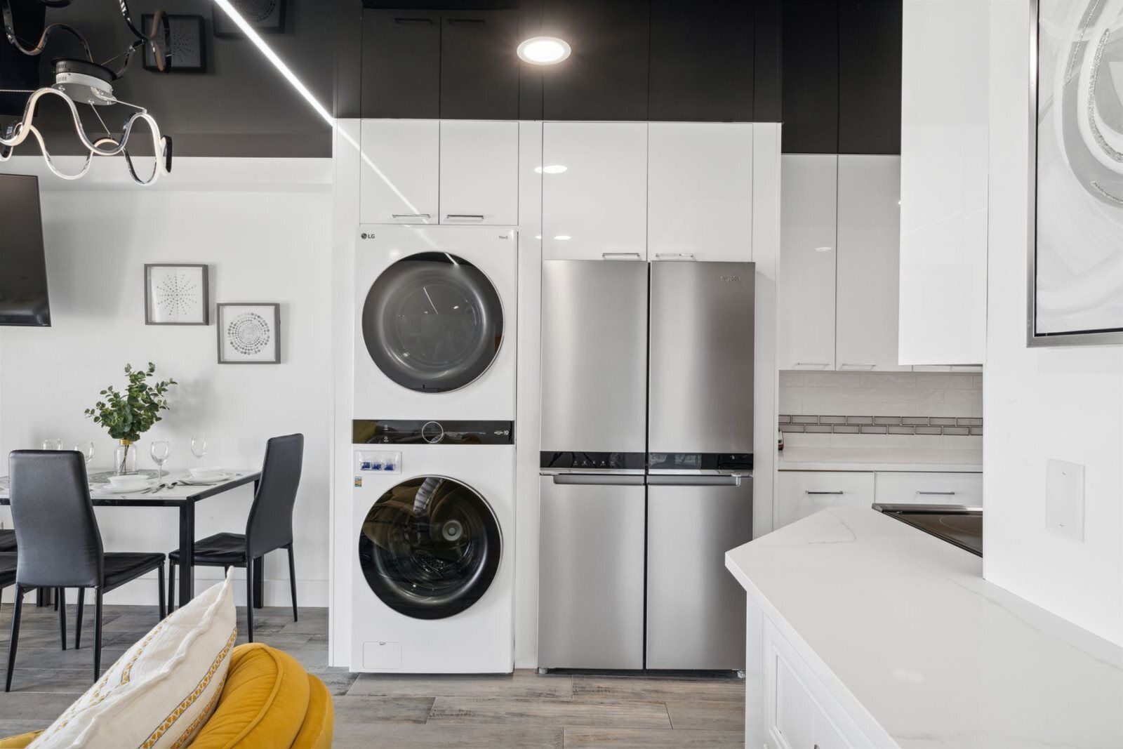 A modern kitchen with white cabinetry, a stainless steel refrigerator, and a built-in washer and dryer.