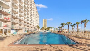 A swimming pool surrounded by lounge chairs, palm trees, and a tall building with balconies. - The Summit 1409 (Panama City Beach)
