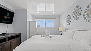 A hotel room with a bed, a TV on a wooden console, a window with blinds, and decorative wall art. - The Summit 1409 (Panama City Beach)