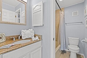 Une salle de bain équipée d’un lavabo, d’un miroir, d’une serviette, d’un rideau de douche et de toilettes.