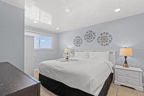 Une chambre à coucher bien aménagée, avec un lit, des tables de chevet, des œuvres d’art décoratives au mur et une fenêtre avec des stores.