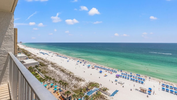 A beach view from a balcony with a clear sky, a sandy beach, and a few umbrellas. - The Summit 1409 (Panama City Beach)