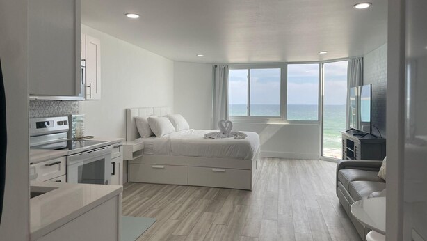 A modern hotel room with a bed, a TV, a sofa, and a view of the ocean. - Top Of The Gulf 815 (Panama City Beach)