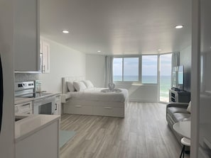 A modern hotel room with a bed, a TV, a sofa, and a view of the ocean.