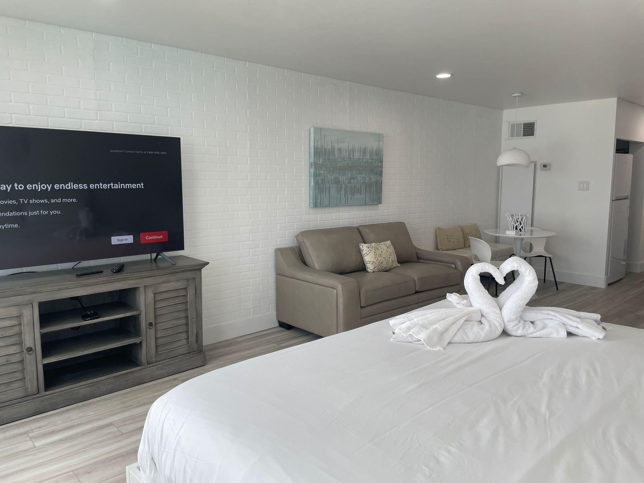 A hotel room with a bed, a TV on a wooden stand, a sofa, a small table, and a wall with a painting.