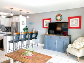 A modern kitchen with white cabinets, a stainless steel refrigerator, and a dining area with a wooden table and bar stools. - The Summit 611 (Panama City Beach)