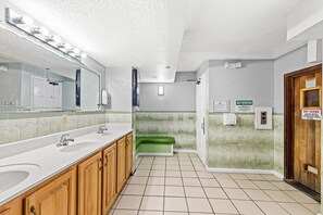 Un baño con dos lavamanos, un espejo con iluminación, un banco verde y un cartel para sauna seca.