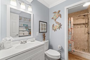Une salle de bain avec un meuble-lavabo blanc, un grand miroir et une douche dotée d’un rideau à motifs.