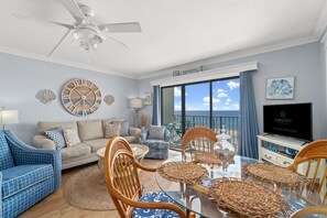A living room with a sofa, chairs, a dining table, a TV, and a balcony with a view. - The Summit 502 (Panama City Beach)