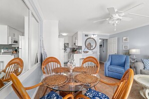 Un coin repas avec une table ronde en verre, des chaises en bois et un ventilateur de plafond.