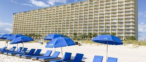 A hotel with multiple balconies and a beach area with sun loungers and umbrellas.