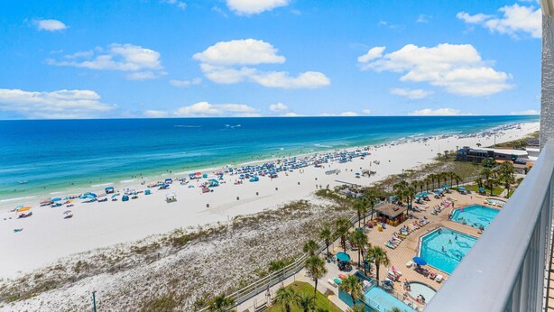 A beach with a pool area, palm trees, and a clear blue sky. - The Summit 1130 (Panama City Beach)