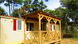 A wooden cabin with a porch, a small deck, and a window with red shutters.