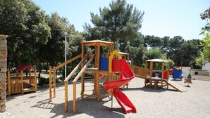 A playground with a red slide, wooden climbing structures, and a covered seating area.