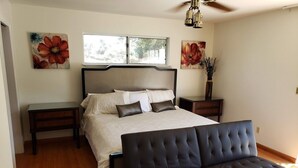 A bedroom with a bed, bedside tables, a sofa, a ceiling fan, and artwork on the walls.