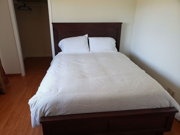 A neatly made bed with a white patterned bedspread and two pillows, a wooden headboard, and a wooden floor. - Yosemite Embassy (Coarsegold)