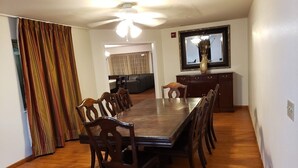 A dining area with a wooden table and chairs, a ceiling fan, and a television on a stand.