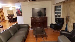 A living room with a sofa set, a coffee table, a TV, and a dining area in the background.
