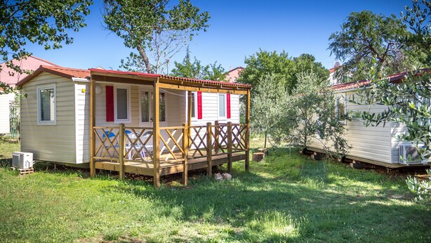 A small, single-story mobile home with a porch and a red roof, surrounded by greenery. - Victoria Mobilehome Camping Imperial (Vodice)