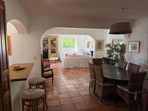 Un coin repas avec une table ronde, des chaises en osier et une vue, par une arche, sur un salon comprenant un canapé et une cheminée.