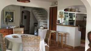 Ein Essbereich mit Korbstühlen und einem Tisch, eine Küche mit Herd und Schränken sowie eine Treppe, die in eine obere Etage führt.