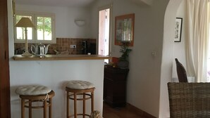Eine Küche mit Holztisch, zwei Barhocker, einem Korbstuhl und einem Esstisch.